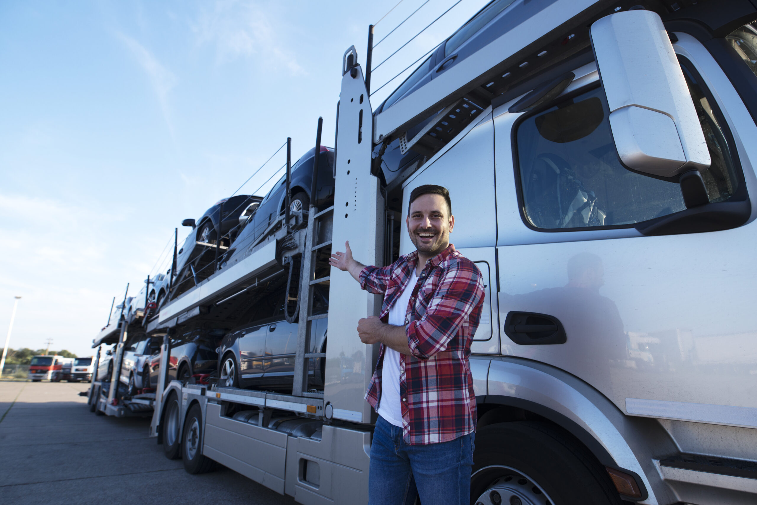 "Middle-aged trucker standing confidently in front of a car hauler loaded with vehicles."